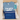 Blue t-shirt with 'I've got a secret' text, blue pouch with baby-related text, and blue carabiner in a box.