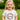 Young girl wearing a white t-shirt with floral design and 'Four' text, standing outdoors.