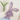 Purple plush bunny toy on a white surface with a vase of flowers in the background