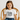 A girl wearing a Santas Helper Black & White  festive Tee shirt sitting on a cane chair